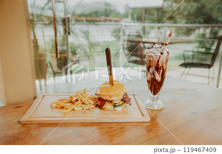 Classic burger with fries and milkshake on wooden board with copy space. Big hamburger with fries and milkshake on restaurant table 119467409
