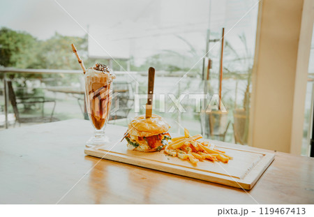 Close up of burger with fries and milkshake on wooden board with space for text. Delicious big burger with french fries and milkshake on restaurant table 119467413