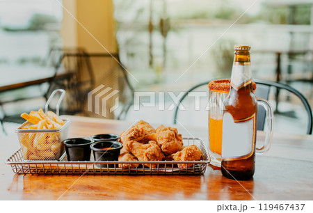 Traditional spicy chicken wings with fries and michelada accompanied with beer served on wooden table 119467437