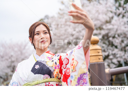 桜の前で自撮りする着物の若い女性 119467477