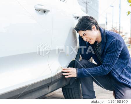 自動車のボディをへこませて落ち込む男性ドライバー 119468109