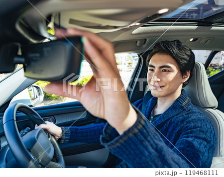 笑顔で自動車のルームミラーを調節する男性ドライバーの車内写真 119468111