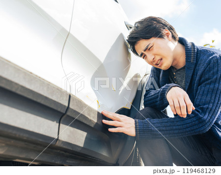 自動車のボディをへこませて落ち込む男性ドライバー 119468129