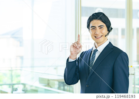 オフィスビルでヘッドセットをつけてお勧めする男性ビジネスパーソン オフィスビルでヘッドセットをつけてお勧めする男性ビジネスパーソン 119468193