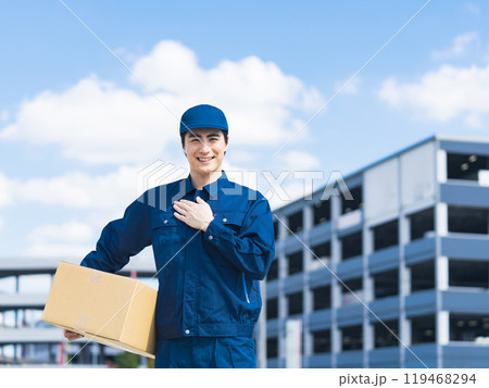 物流センターのような建物の前で荷物を持って胸に手を当てるデリバリースタッフ 119468294