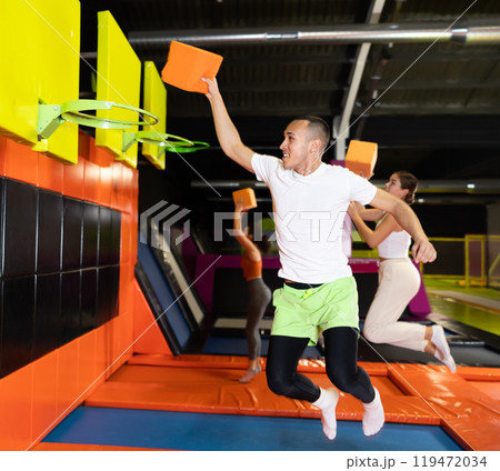 Cheerful man playing basketball with foam cube at trampoline park Cheerful man playing basketball with foam cube at trampoline park 119472034