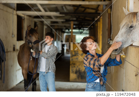 Female owner of horse visits animal in stable, strokes its muzzle, 119472048