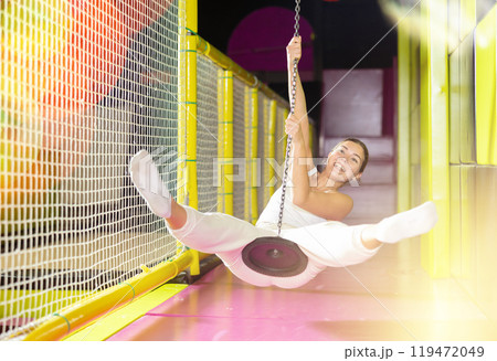 Laughing girl enjoying swing ride on zipline at indoor entertainment venue 119472049