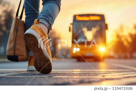 A person walking toward a bus during sunset, with a warm glow illuminating the scene. 119472086