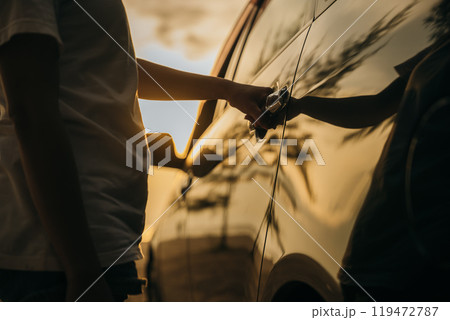 Close up young woman hand opening opening the door of a car at sunset. Hand holding door hand to open to get into driver seat. Travel road trip concept 119472787
