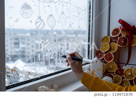Sustainable responsible holiday decor. Female hand painting advent candles painted on window glass indoor at home. Christmas winter decoration. White pattern. Snow art tracery on season. Diy 119472876