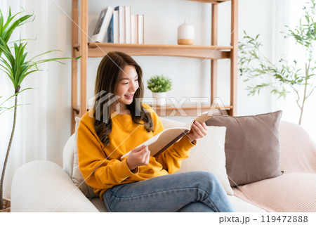 Young beautiful Asian woman reading a book on couch at home Young beautiful Asian woman reading a book on couch at home 119472888
