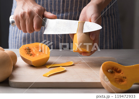 Woman hand holding kitchen knife and peeling butternut squash, Homemade cooking 119472933