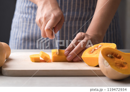 Woman hand holding kitchen knife and cutting butternut squash on wooden board, Homemade cooking 119472934