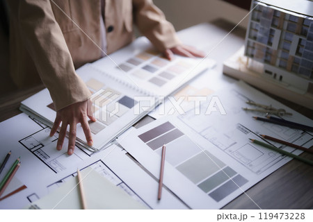 Female architect choosing color swatch sample to design interior of building project on blueprint Female architect choosing color swatch sample to design interior of building project on blueprint 119473228
