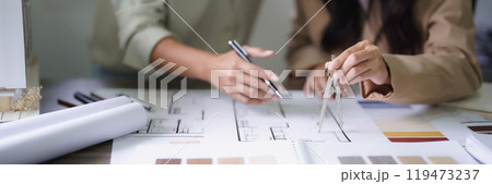 Two female architects discuss interior design building project and use divider compass on blueprint 119473237