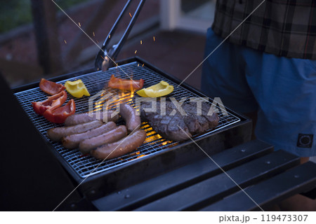 グランピング施設のバーベキューコンロで食材を焼く男性手元 グランピング施設のバーベキューコンロで食材を焼く男性手元 119473307