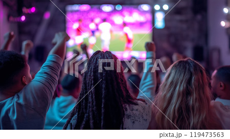 A group of fans cheer while watching a live sports event on a big screen, celebrating a moment of excitement together. A group of fans cheer while watching a live sports event on a big screen, celebrating a moment of excitement together. 119473563