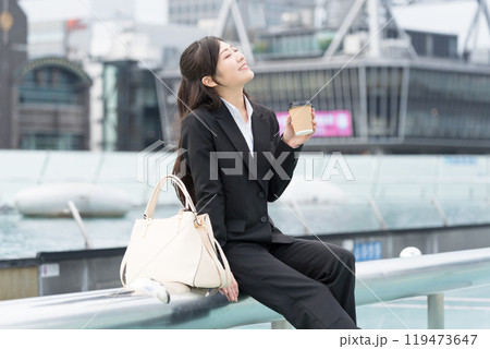 都会の真ん中でテイクアウトコーヒーを飲んでくつろぐ若いビジネスウーマン 都会の真ん中でテイクアウトコーヒーを飲んでくつろぐ若いビジネスウーマン 119473647