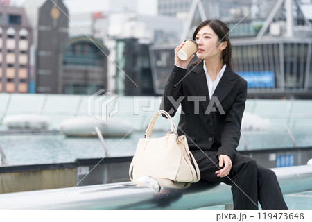 都会の真ん中でテイクアウトコーヒーを飲んでくつろぐ若いビジネスウーマン 都会の真ん中でテイクアウトコーヒーを飲んでくつろぐ若いビジネスウーマン 119473648