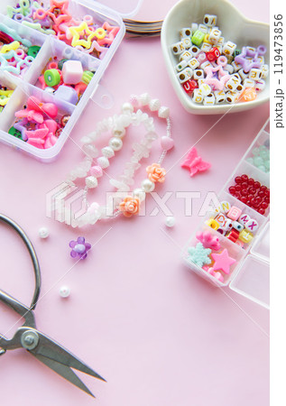 Crafting colorful beaded jewelry on a pastel pink workspace Crafting colorful beaded jewelry on a pastel pink workspace 119473856