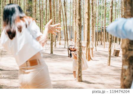 Asian family father and mother playing hide and seek back tree with daughter on forest nature park, happy parents funny together, Family enjoying moment of holiday 119474204