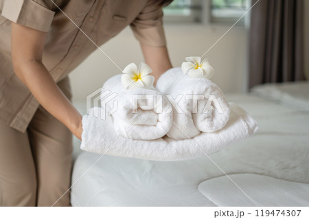 A hotel maid stacked towels on the bed and placed flowers on the towels in a hotel room A hotel maid stacked towels on the bed and placed flowers on the towels in a hotel room 119474307