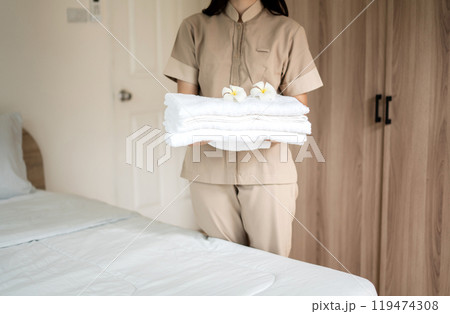 A hotel maid stacked towels on the bed and placed flowers on the towels in a hotel room A hotel maid stacked towels on the bed and placed flowers on the towels in a hotel room 119474308