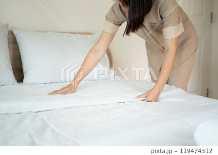 The hotel maid cleans and makes the bed in the hotel room The hotel maid cleans and makes the bed in the hotel room 119474312