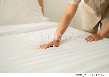 The hotel maid cleans and makes the bed in the hotel room 119474877