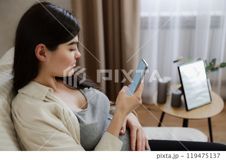 Young pregnant woman with baby belly using her mobile cell phone 119475137