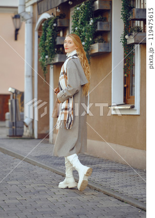 Young woman in a stylish coat strolls along a quaint cobblestone street in autumn Young woman in a stylish coat strolls along a quaint cobblestone street in autumn 119475615