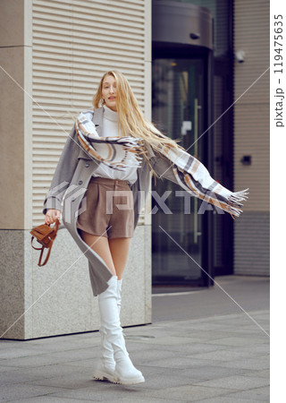 A joyful woman stands playfully on a city sidewalk in trendy autumn outfit A joyful woman stands playfully on a city sidewalk in trendy autumn outfit 119475635