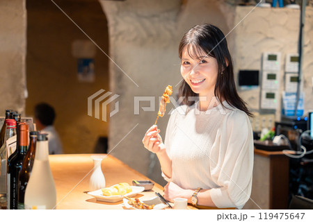 一人でカウンター席に座って焼き鳥を食べる女性 119475647