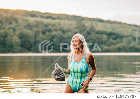 Cold water swimming for elderly women. Portrait of senior sporty women standing in lake during cold morning. 119475787