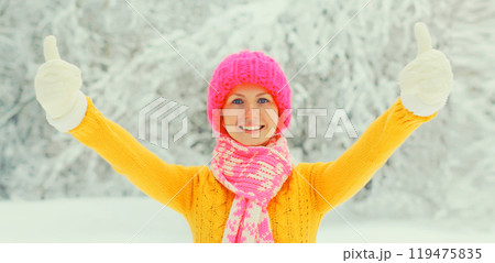 Happy cheerful smiling young woman in colorful knitted hat, enjoys weather in winter snowy park 119475835