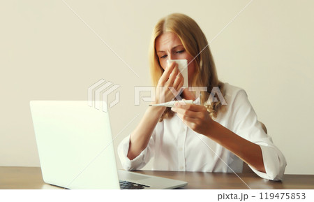 Sick woman sneezing blow nose, measuring body temperature with thermometer working with laptop 119475853