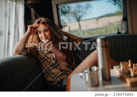 Young beautiful woman is on a camping trip in nature, sitting in her caravan and enjoying morning cup of coffee. Young beautiful woman is on a camping trip in nature, sitting in her caravan and enjoying morning cup of coffee. 119475893