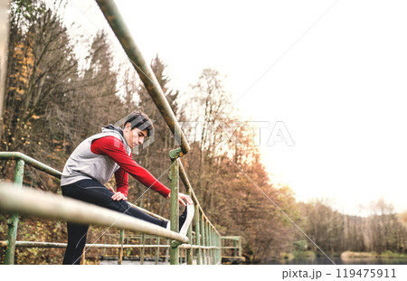Sporty man stretching his legs before run, standing on bridge in park. Morning workout for young man. 119475911