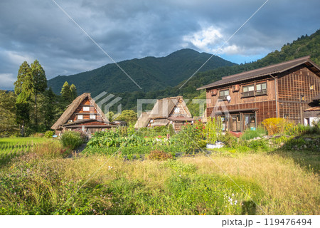 Shirakawa village, Gifu, Japan. A picturesque rural scene featuring traditional wooden houses surrounded by vibrant greenery and mountains under a cloudy sky. Shirakawa village, Gifu, Japan. A picturesque rural scene featuring traditional wooden houses surrounded by vibrant greenery and mountains under a cloudy sky. 119476494