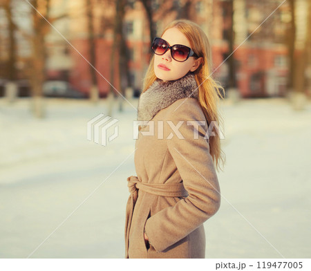 Beautiful blonde young woman posing in sunglasses, winter coat outdoors in park 119477005