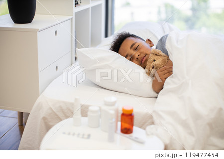 Comforting scene of a sick African boy resting in bed Comforting scene of a sick African boy resting in bed 119477454