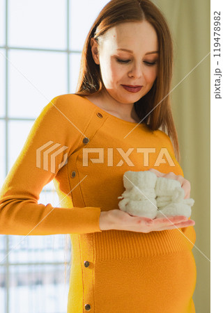 Pregnancy motherhood people expectation future. Pregnant woman with big belly holding newborn baby booties smiling at home. Young mom enjoying pregnancy. Maternity tenderness parenthood new life 119478982