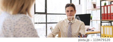 Young economist looks at woman sitting at table by clipboard Young economist looks at woman sitting at table by clipboard 119479120