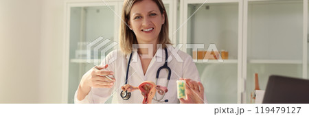 Lady gynecologist holds bottle of pills looking in camera 119479127