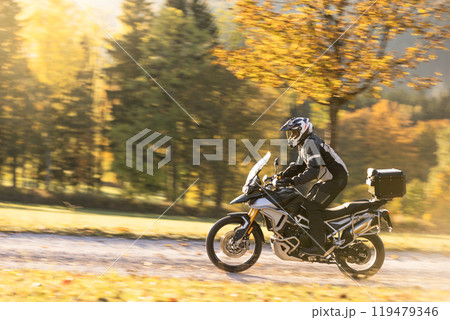 Motorcyclist rides through scenic autumn forest trail. Motorcyclist rides through scenic autumn forest trail. 119479346