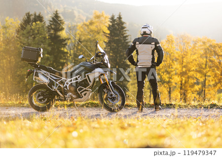 Motorcyclist stays in scenic autumn forest trail. Motorcyclist stays in scenic autumn forest trail. 119479347