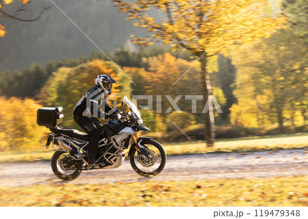 Motorcyclist rides through scenic autumn forest trail. Motorcyclist rides through scenic autumn forest trail. 119479348
