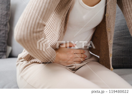 A woman is sitting on a couch with a stomach ache 119480022