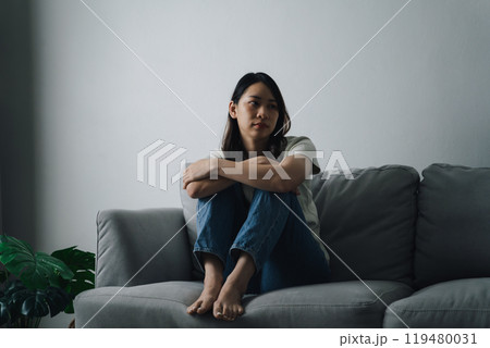 Unhappy lonely depressed woman is sitting on the couch. She looks sad and tired. Unhappy lonely depressed woman is sitting on the couch. She looks sad and tired. 119480031